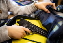 Kid placing handgun inside a backpack on desk