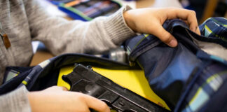 Kid placing handgun inside a backpack on desk