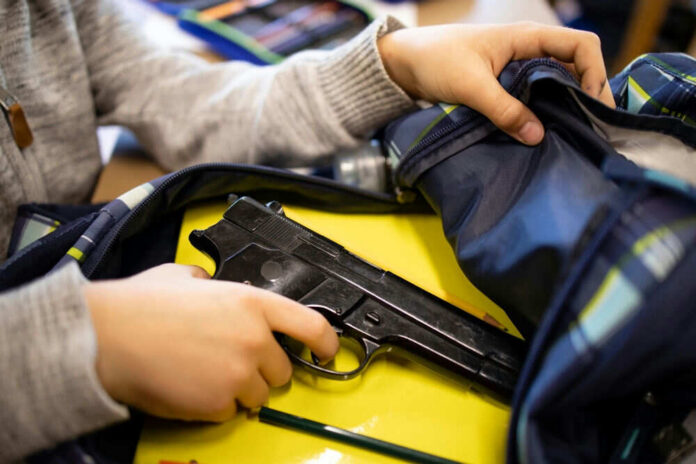 Kid placing handgun inside a backpack on desk