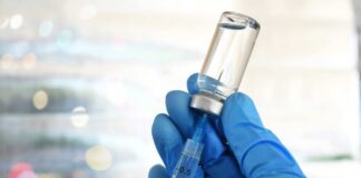 A gloved hand holding a syringe and a vial of liquid