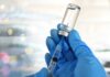 A gloved hand holding a syringe and a vial of liquid