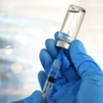 A gloved hand holding a syringe and a vial of liquid