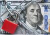A red padlock and chain over a hundred dollar bill featuring Benjamin Franklin