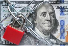 A red padlock and chain over a hundred dollar bill featuring Benjamin Franklin
