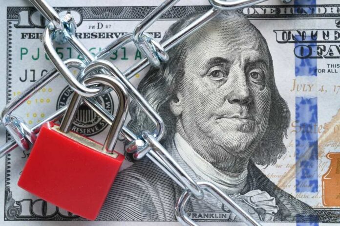A red padlock and chain over a hundred dollar bill featuring Benjamin Franklin