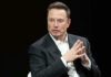 Man in suit, hands clasped, black background.