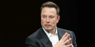 Man in suit, hands clasped, black background.