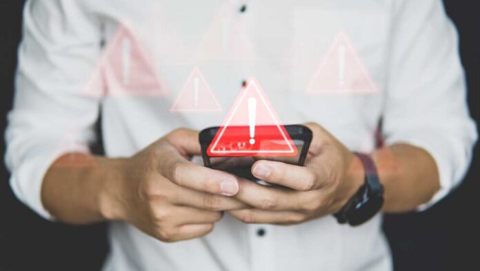 Emergency,Warning,Alert,Alarm,On,Smartphone,,Data,Network,Protection,,Virus Hands holding a smartphone with warning icons overlay