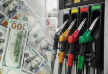 Fuel pump nozzles next to spread of U.S. hundred-dollar bills