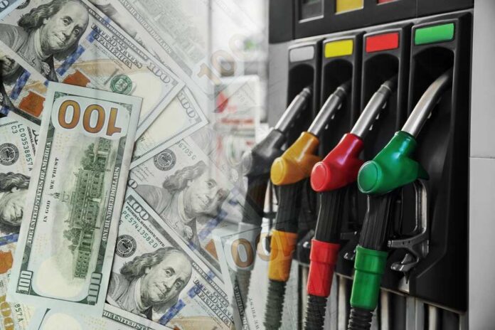 Fuel pump nozzles next to spread of U.S. hundred-dollar bills