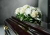 A floral arrangement of white roses and greenery on a polished casket