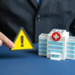 A business professional holding a warning sign next to a model of a hospital