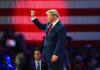 Donald Trump raises a fist on stage before a large U.S. flag