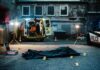 Police investigation at a crime scene with a covered body and evidence markers