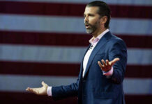 Donald Trump Jr. speaking on stage with an American flag backdrop