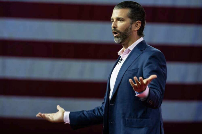 Donald Trump Jr. speaking on stage with an American flag backdrop