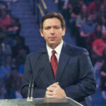 Ron DeSantis at a podium during an event; Christian Jones not visible