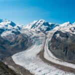 Glacier winding through snow-capped alpine mountains under a clear blue sky