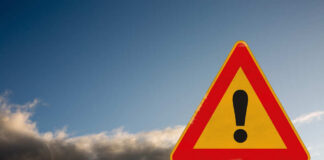 A triangular warning sign with an exclamation mark against a cloudy sky