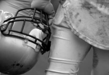 Football player holding helmet, dirty uniform close-up.