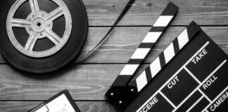 Film reel, storyboard, and clapperboard on wooden surface.