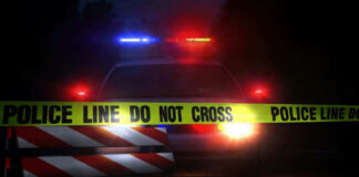 Police car with flashing lights behind caution tape.
