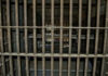 Empty, rusty barred jail cell with metal bunks.