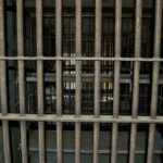 Empty, rusty barred jail cell with metal bunks.