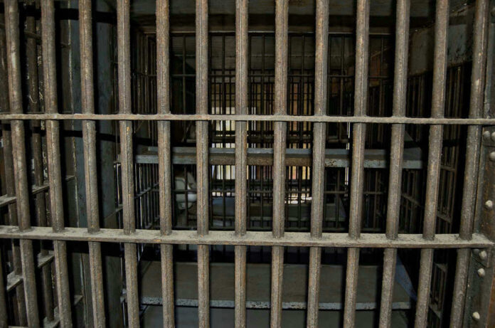 Empty, rusty barred jail cell with metal bunks.