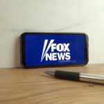 Smartphone displaying the Fox News logo on a wooden surface