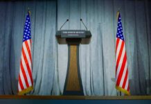Defiant Gambit: Emanuel Dares Voters Podium between two American flags on a stage