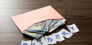 Envelope with cash and notes spelling bribery on wooden table