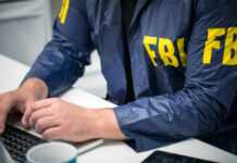 Person in FBI jacket working on laptop.